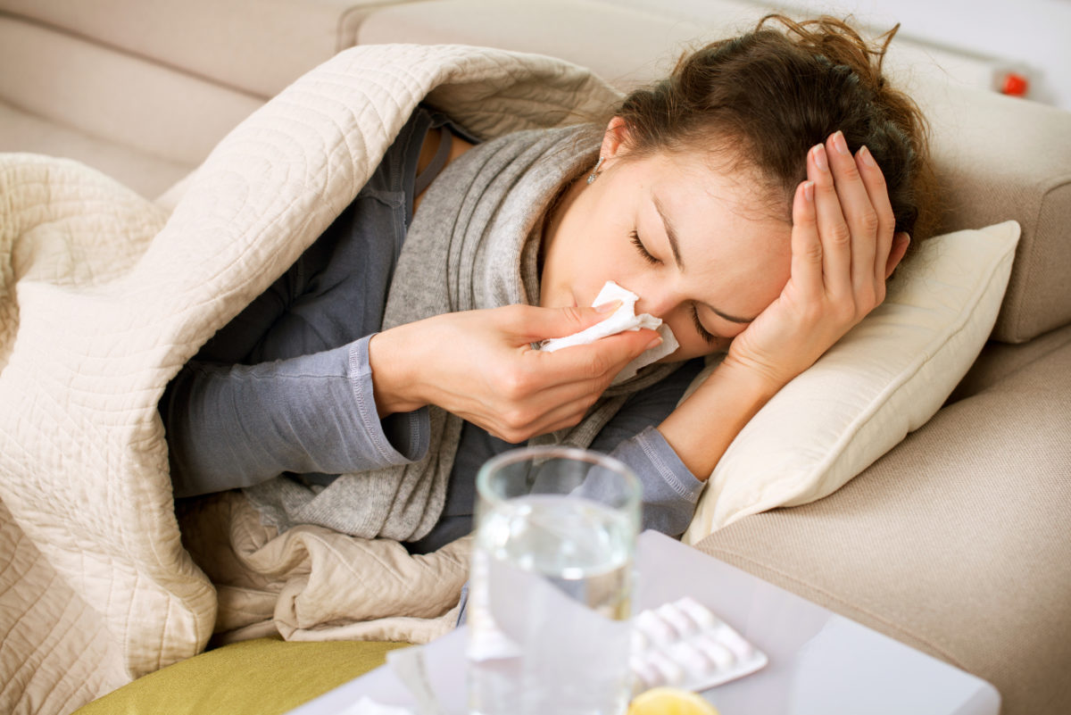 woman sick blowing her nose on the couch